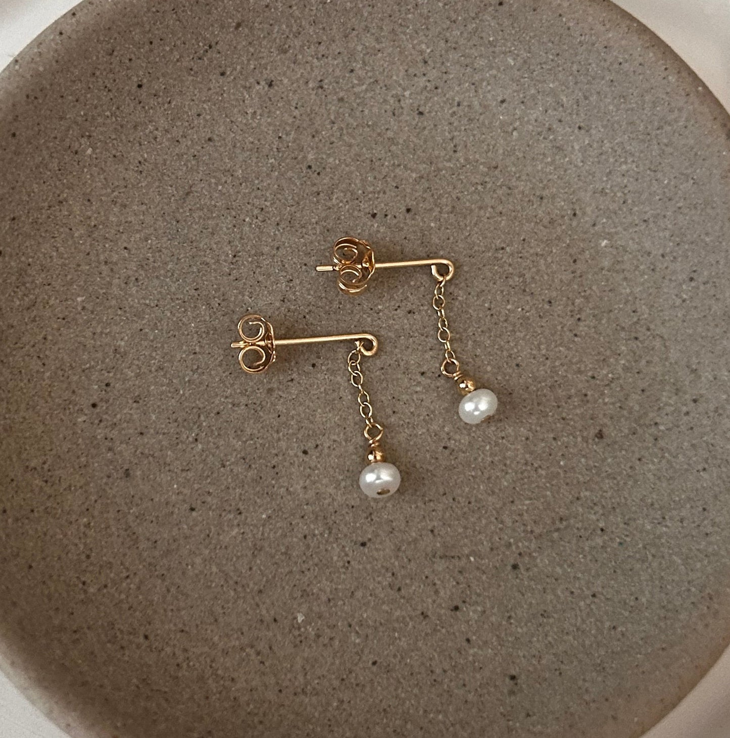 Gold earrings with pearls on a textured stone surface inside a white dish.