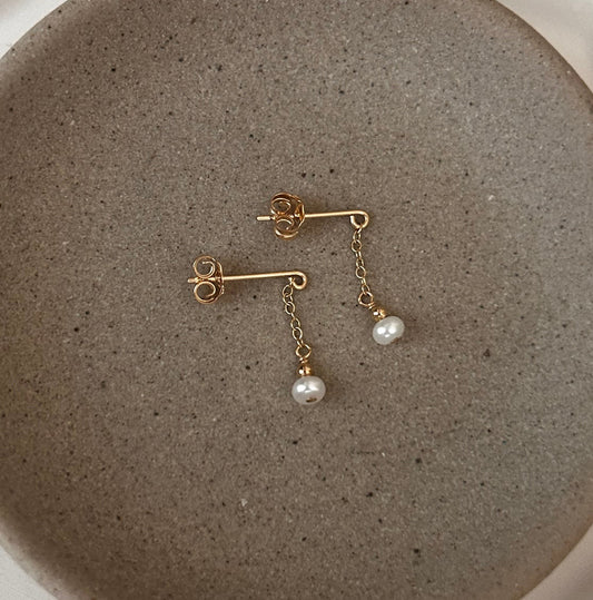 Gold earrings with pearls on a textured stone surface inside a white dish.